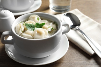 Photo of Bowl of tasty dumplings in broth served on wooden table, space for text