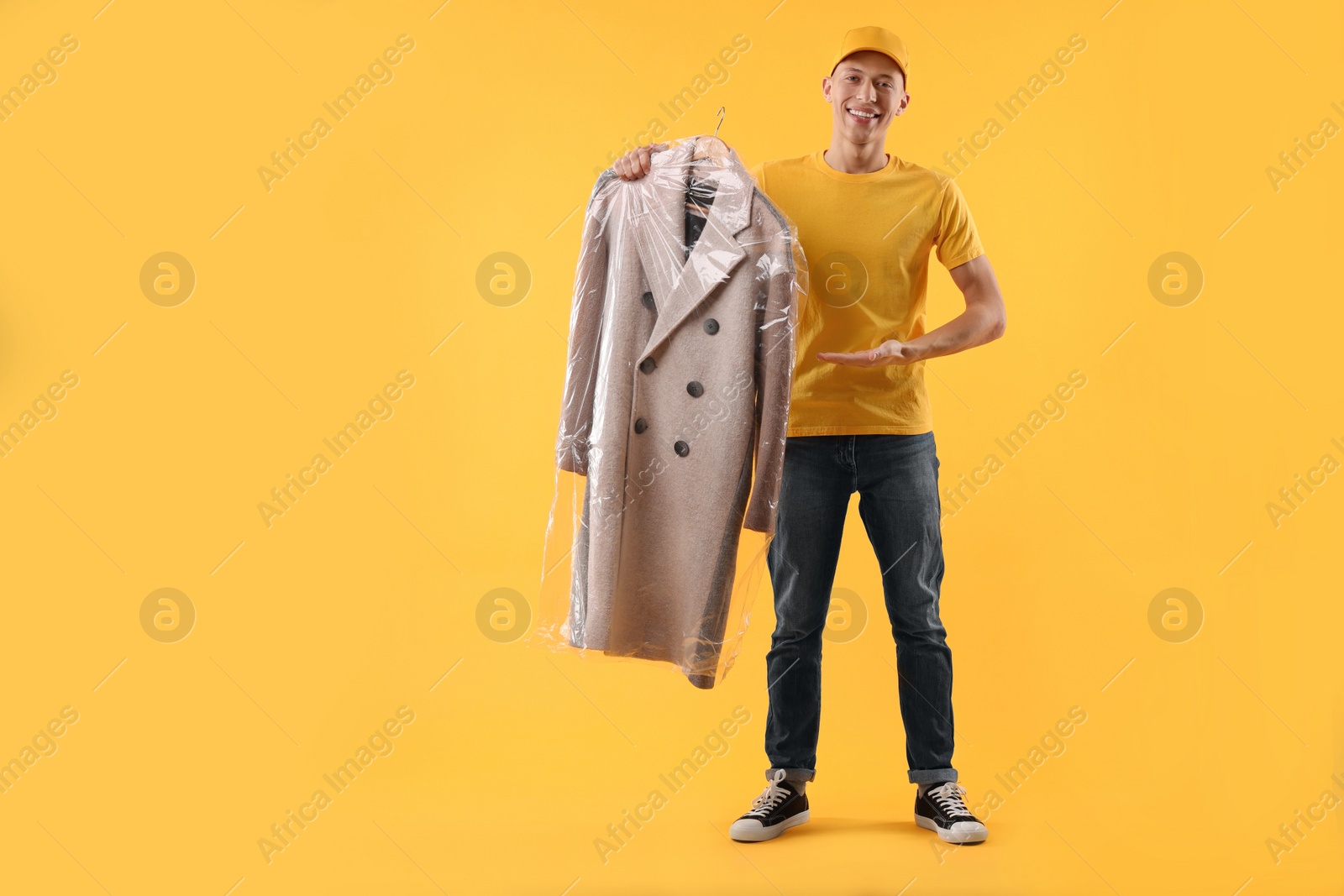 Photo of Dry-cleaning delivery. Happy courier holding coat in plastic bag on orange background, space for text