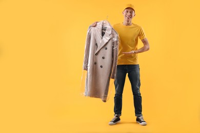 Dry-cleaning delivery. Happy courier holding coat in plastic bag on orange background, space for text