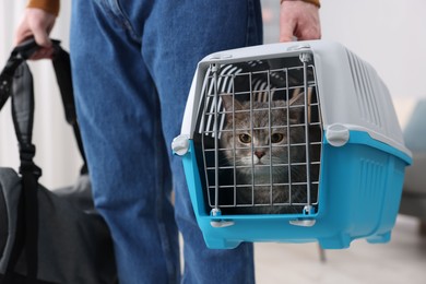 Travel with pet. Man holding carrier with cute cat and bag indoors, closeup