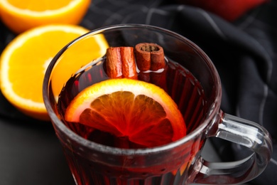 Photo of Glass cup of tasty mulled wine on black table, closeup