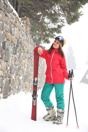 Photo of Young woman with skis wearing winter sport clothes outdoors