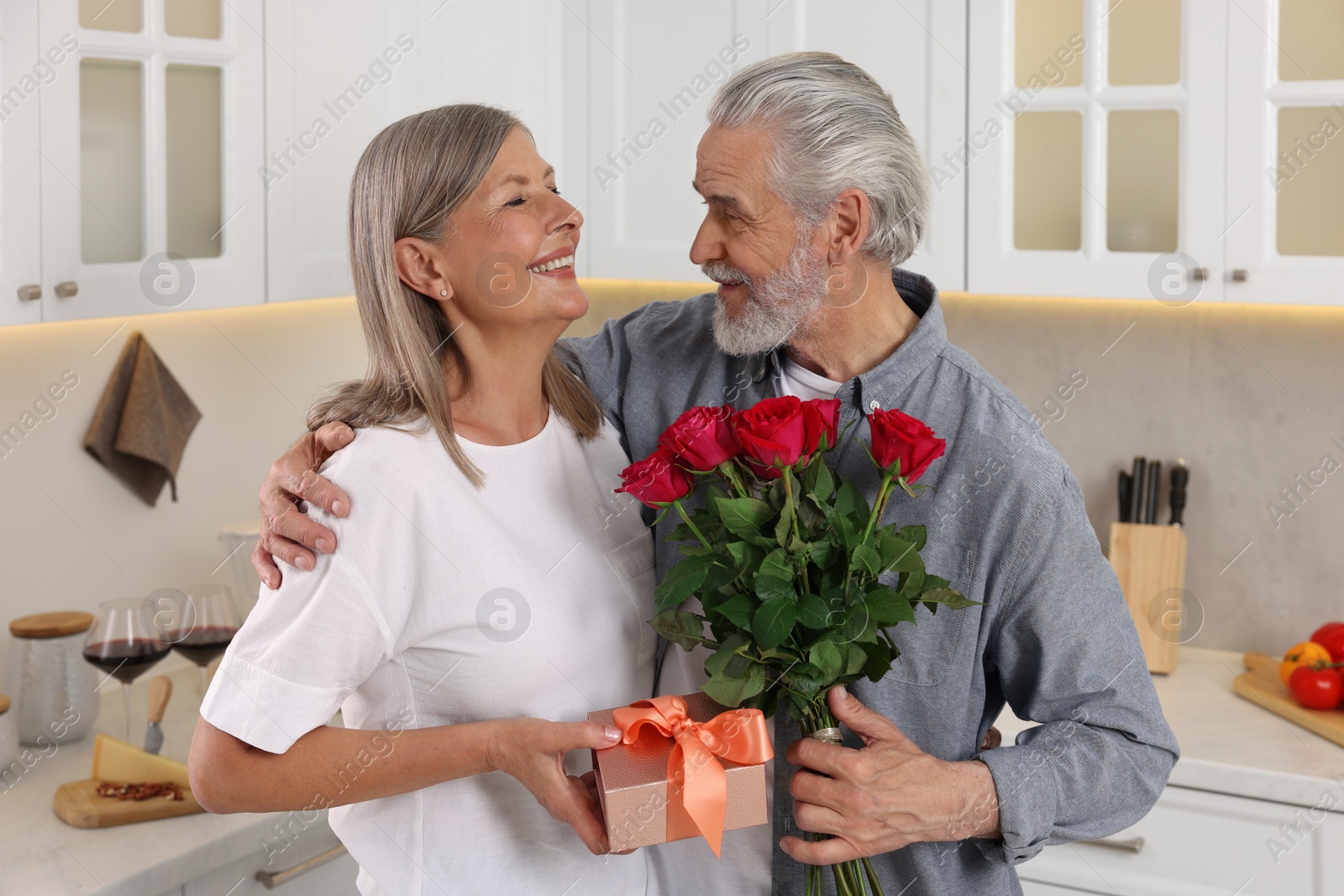 Photo of Happy affectionate senior couple with gift box and beautiful bouquet indoors