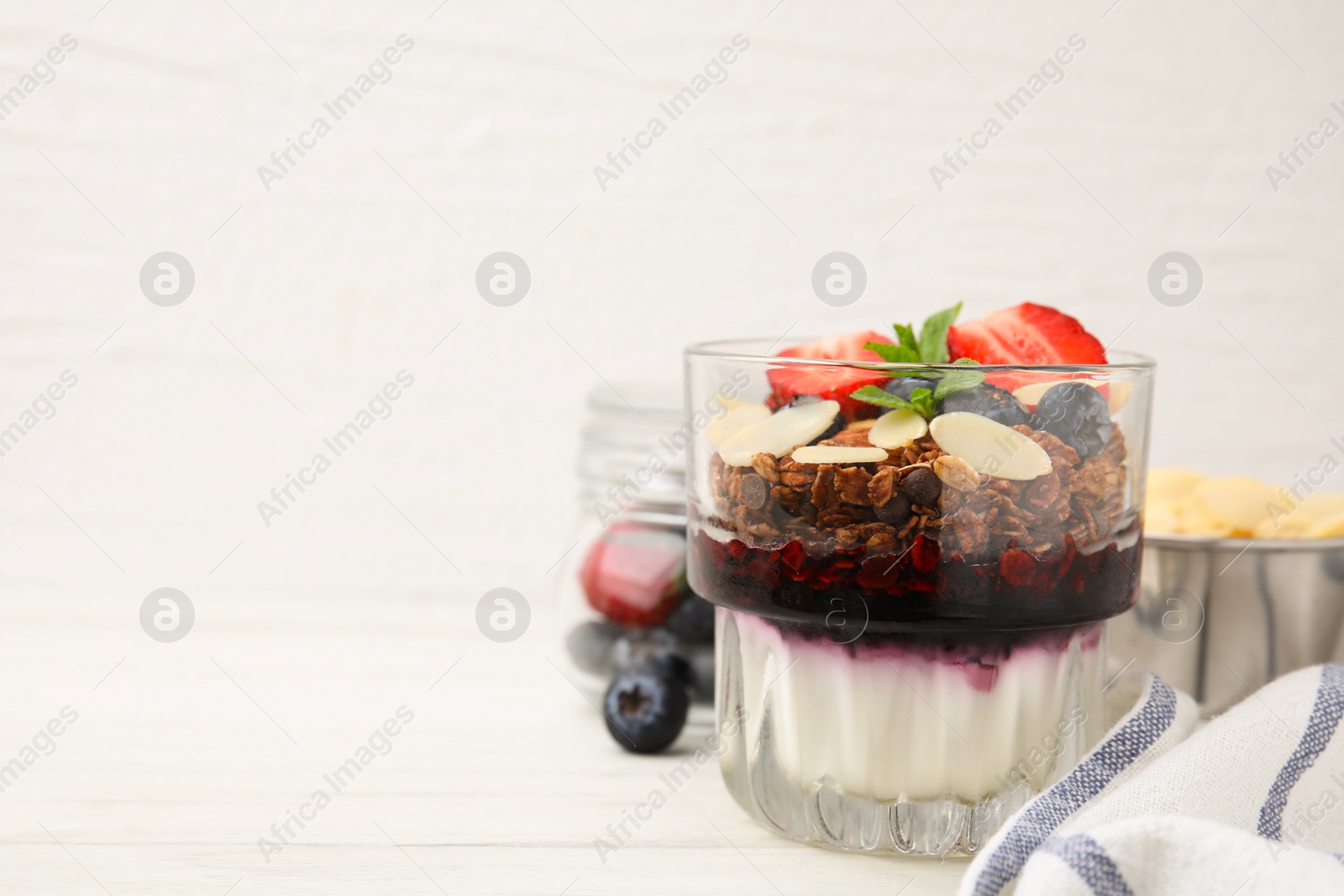 Photo of Tasty granola with berries, jam, yogurt and almond flakes in glass on white table. Space for text