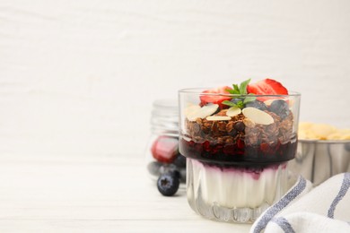 Photo of Tasty granola with berries, jam, yogurt and almond flakes in glass on white table. Space for text