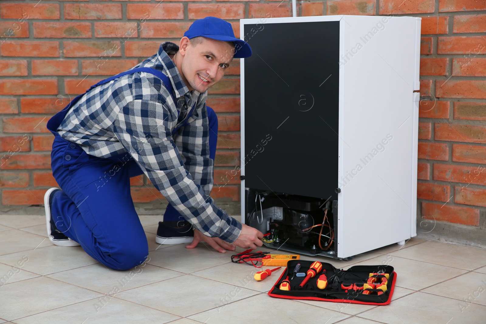 Photo of Male technician in uniform repairing refrigerator indoors