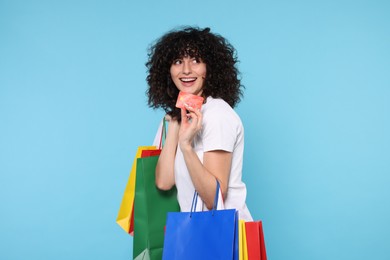 Happy young woman with shopping bags and credit cards on light blue background