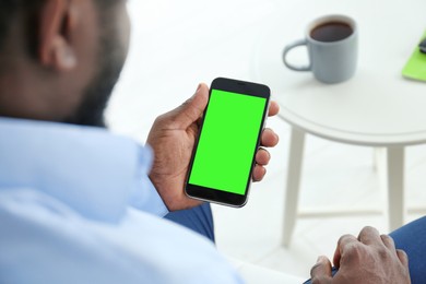 Chroma key compositing. African American man holding smartphone with green screen indoors, closeup. Mockup for design
