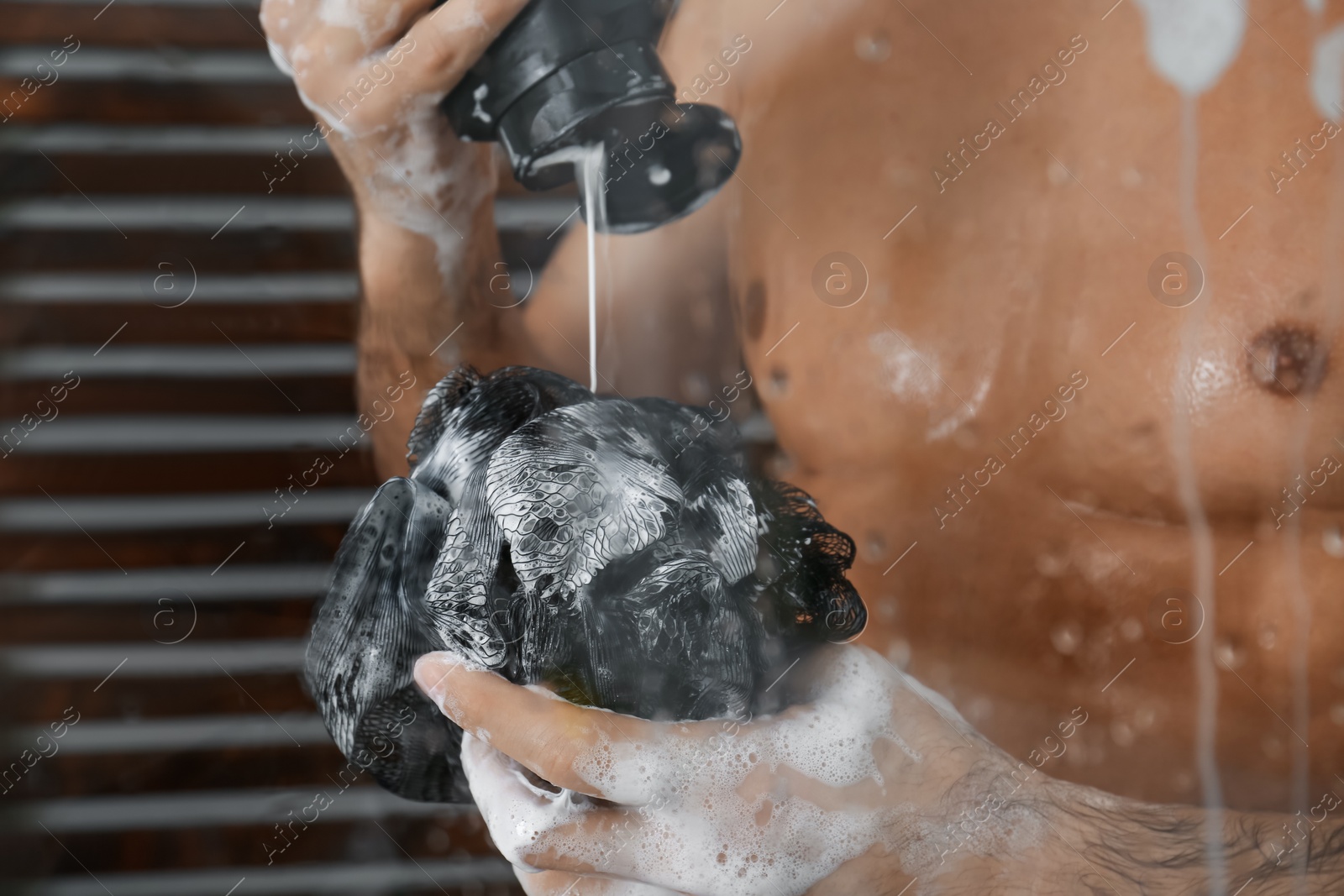 Photo of Man applying gel onto mesh pouf in shower at home, closeup