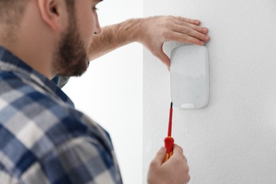 Photo of Man installing security alarm system on light wall at home, closeup