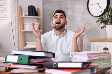 Overwhelmed man surrounded by documents at workplace in office