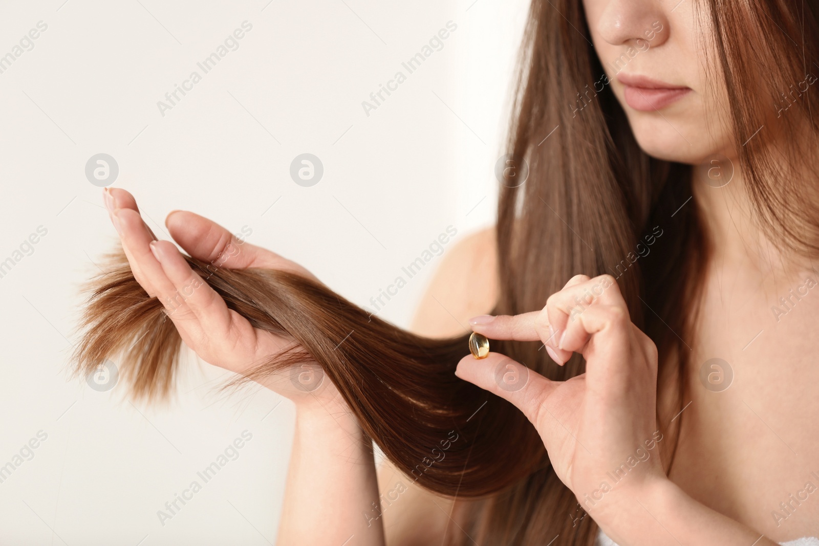 Photo of Woman holding vitamin capsule for hair health on light background, closeup