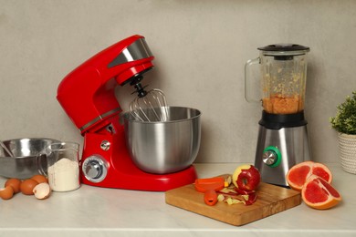 Photo of Modern red stand mixer, blender and different ingredients on white marble table