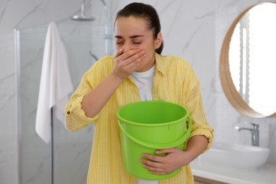 Photo of Young woman with bucket suffering from nausea in bathroom. Food poisoning