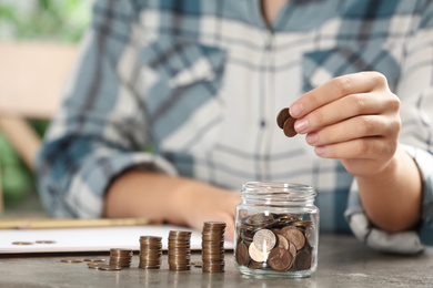 Photo of Woman putting money into glass jar at table, closeup