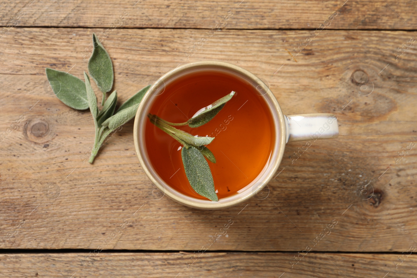 Photo of Cup of aromatic sage tea and fresh leaves on wooden table, flat lay