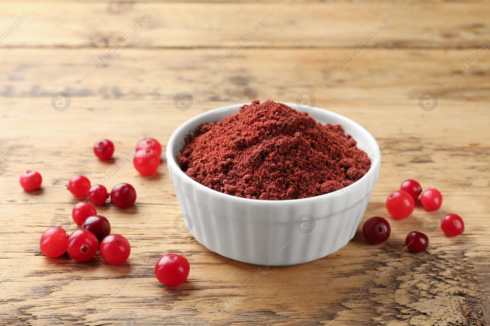 Photo of Dried cranberry powder in bowl and fresh berries on wooden table