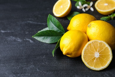 Many fresh ripe lemons with green leaves on black table, closeup. Space for text