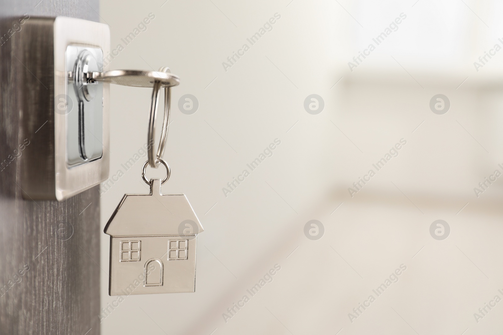 Photo of Mortgage and real estate. Open door with key and house shaped keychain against blurred background, space for text