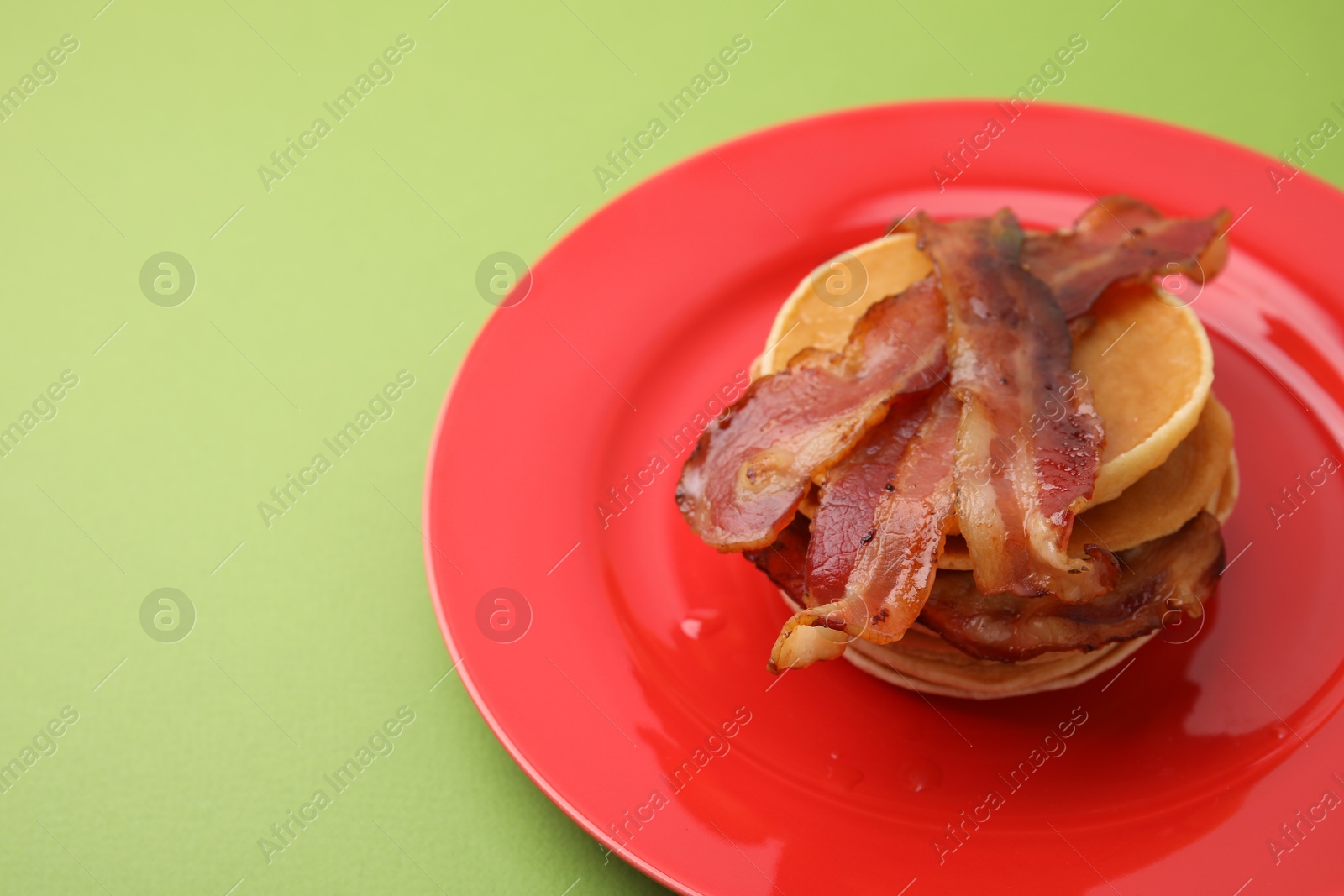 Photo of Delicious pancakes with bacon on green table, closeup. Space for text