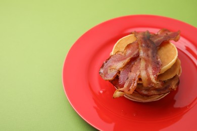 Delicious pancakes with bacon on green table, closeup. Space for text