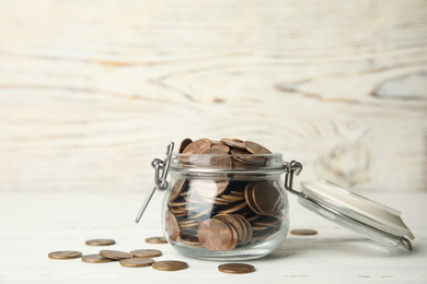 Glass jar with coins on white wooden table