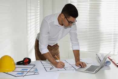 Architect working with construction drawings and laptop in office