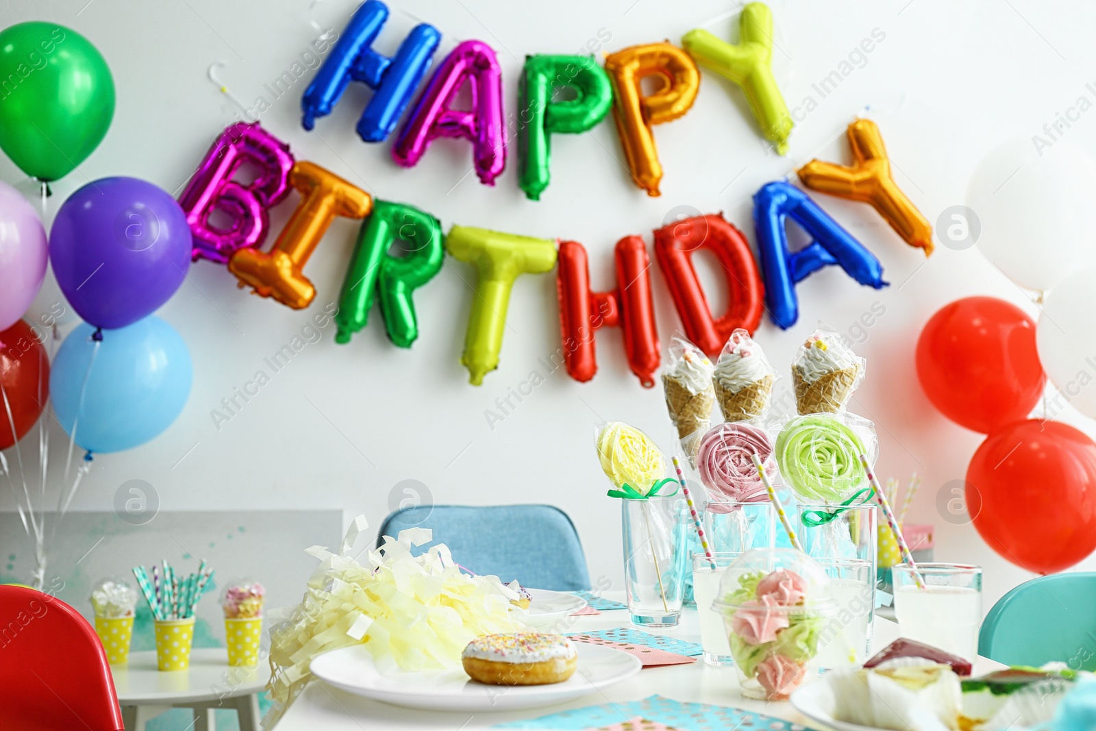 Photo of Table with treats and phrase HAPPY BIRTHDAY made of colorful balloon letters in living room