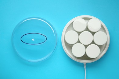 Modern yogurt maker with jars on light blue background, flat lay