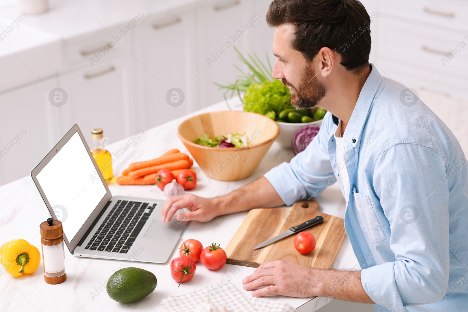 Photo of Man making dinner while watching online cooking course via laptop in kitchen