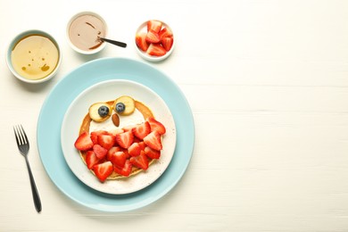 Photo of Creative serving for kids. Plate with cute owl made of pancakes, strawberries, cream, banana and almond on white wooden table, flat lay. Space for text