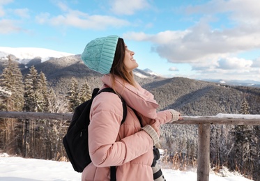 Young woman with backpack and camera enjoying mountain view during winter vacation