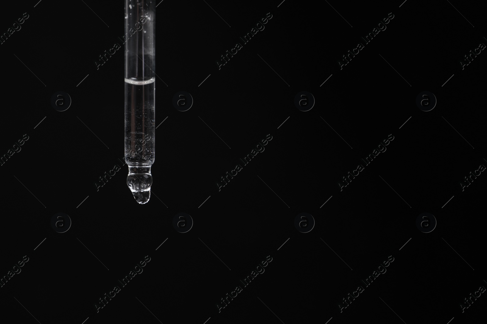 Photo of Dripping cosmetic serum from pipette against black background, space for text