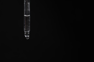 Photo of Dripping cosmetic serum from pipette against black background, space for text