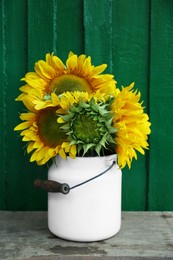 Bouquet of beautiful sunflowers in tin on wooden table near green wall