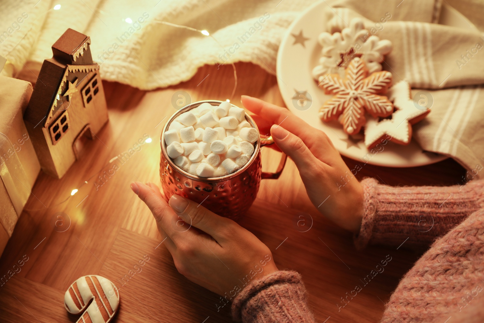 Photo of Woman holding cup of hot drink with marshmallows at wooden table, above view. Magic Christmas atmosphere