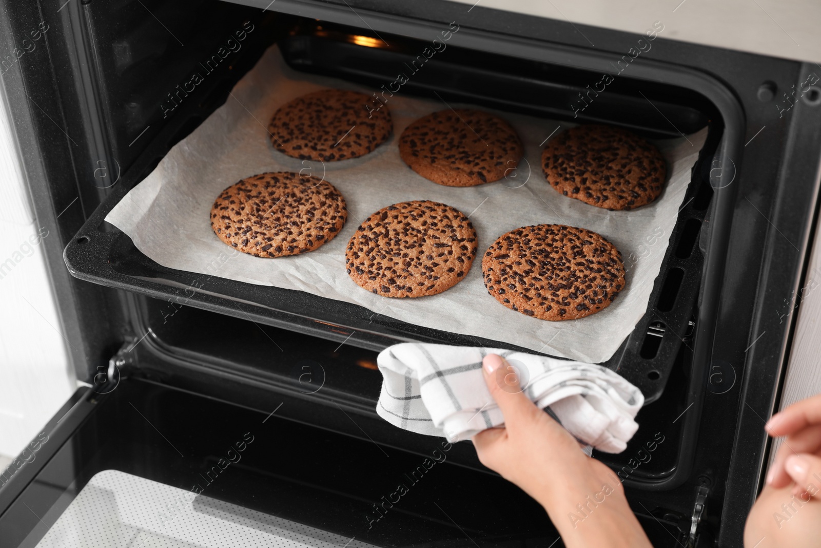 Photo of Young woman taking baking sheet with cookies from oven, closeup