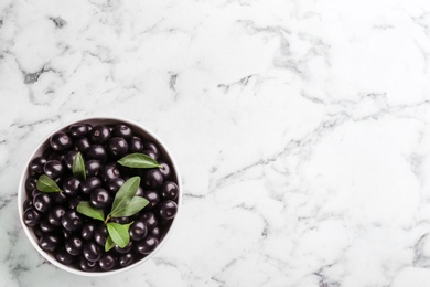 Fresh acai berries in bowl on white marble table, top view. Space for text