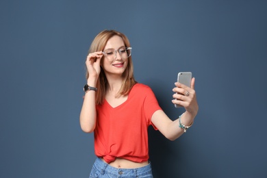 Attractive young woman taking selfie on color background