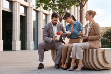 Business lunch. Happy colleagues spending time together during break on bench outdoors