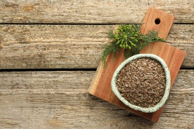 Photo of Board with bowl of dry seeds and fresh dill on wooden table, top view. Space for text