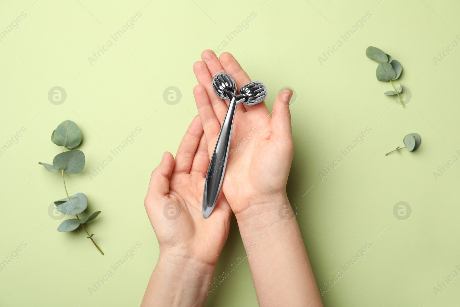 Photo of Woman with metal face roller on green background, top view
