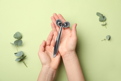 Woman with metal face roller on green background, top view