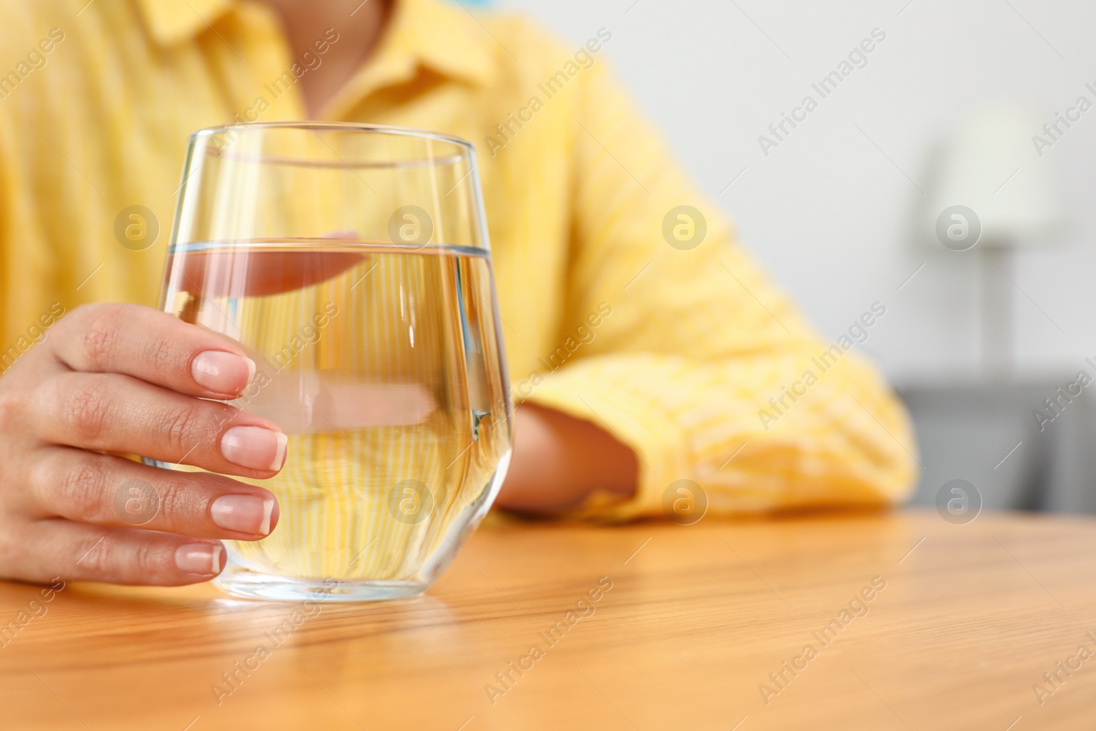 Photo of Woman holding glass of water at wooden table, closeup with space for text. Refreshing drink