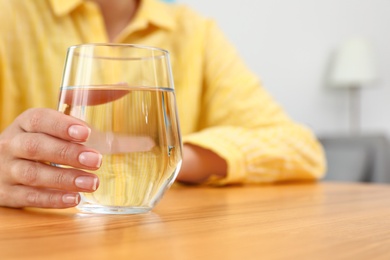 Woman holding glass of water at wooden table, closeup with space for text. Refreshing drink