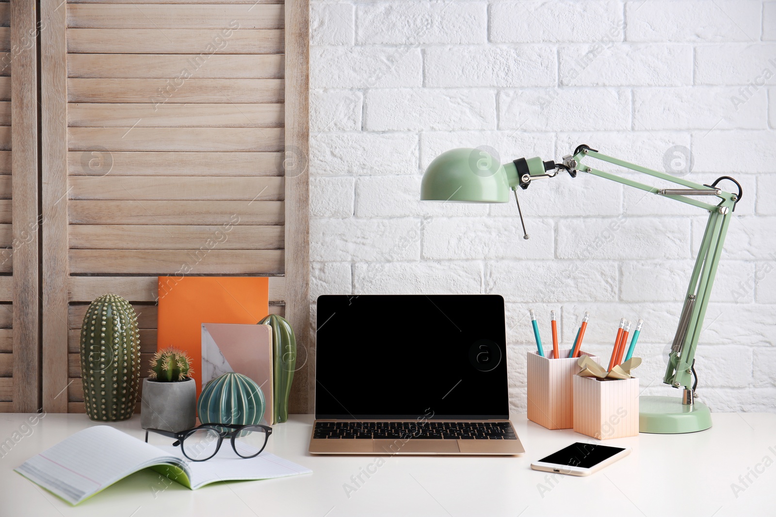 Photo of Modern workplace with laptop on table against brick wall. Mockup for design