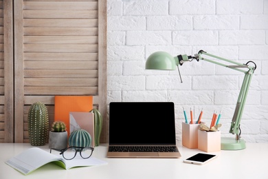 Modern workplace with laptop on table against brick wall. Mockup for design