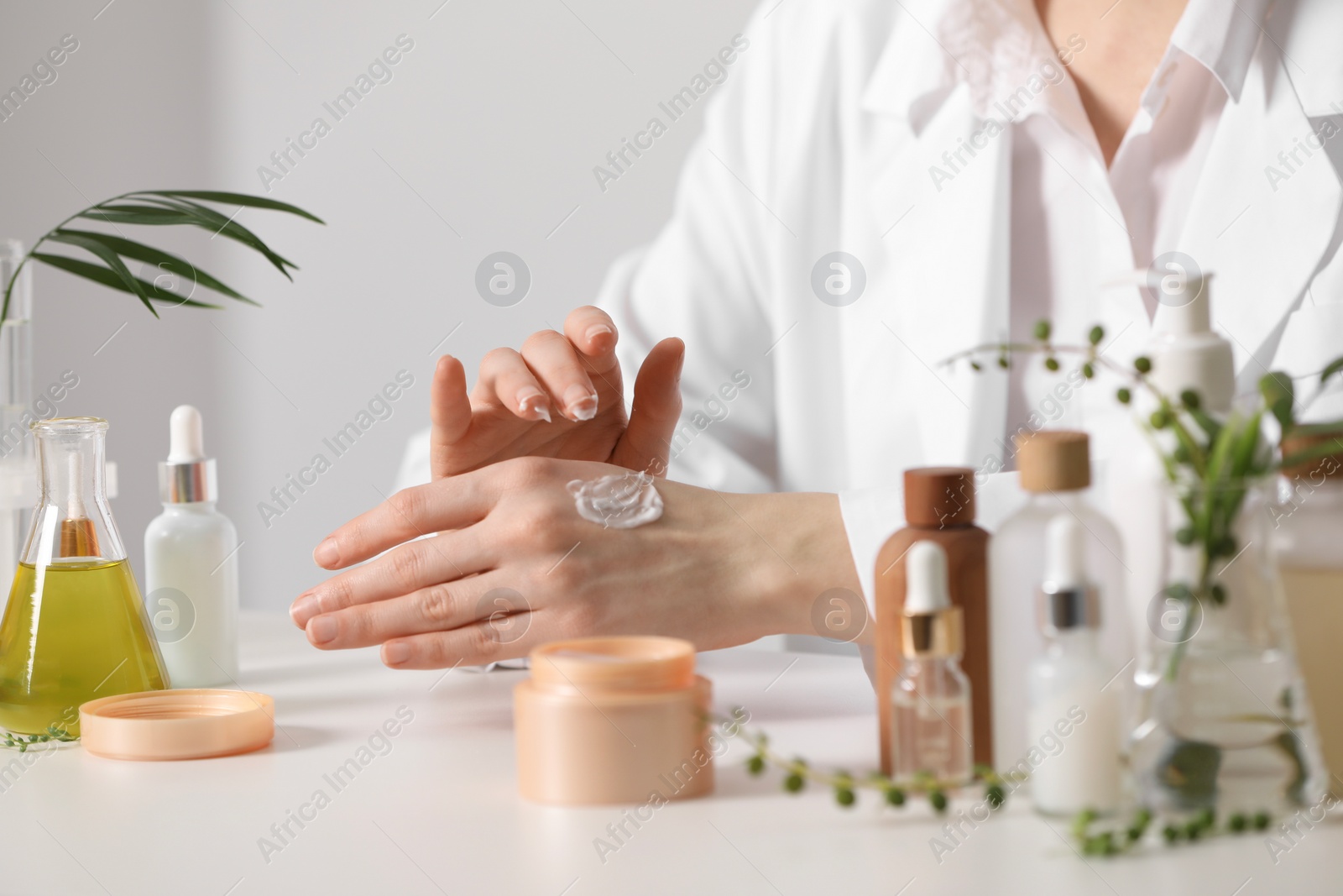 Photo of Dermatologist applying cream onto hand at white table indoors, closeup. Testing cosmetic product