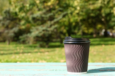 Cardboard coffee cup on wooden table outdoors. Space for text