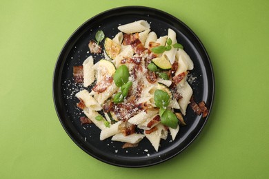 Tasty pasta with bacon and basil on light green table, top view